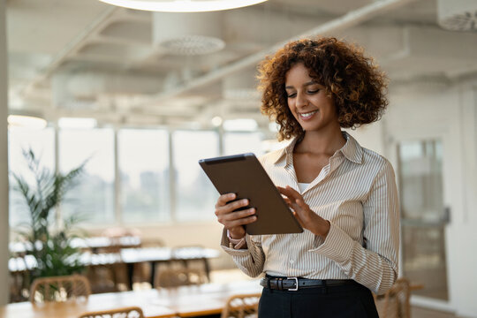 Smiling middle eastern business woman browsing on digital tablet in coworking office workplace, using touchscreen. In 30s, female agent works as banker, broker, accountant, employee. Copy space