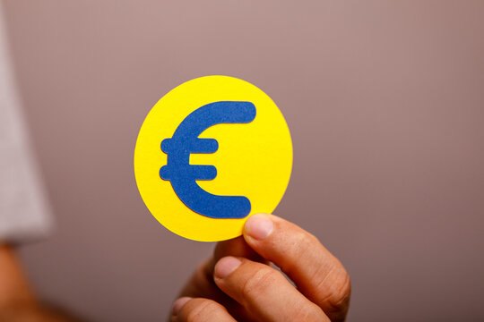 A person's hand holds a vibrant yellow circle featuring a blue Euro currency symbol.