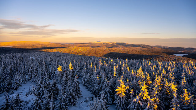 Sunset illuminates the winter landscape of Jizera Mountains and Giant Mountains. Snow covers the trees as evening approaches, creating a warm glow in the valley.