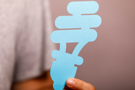 A person holds a light blue paper cutout symbolizing an energy-efficient light bulb, promoting