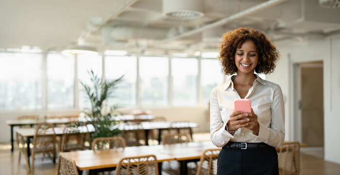 Web banner of smiling indian business woman texting on mobile phone in coworking office workplace, using smartphone app. In 30s, female employee works as staff, worker, professional. Copy space