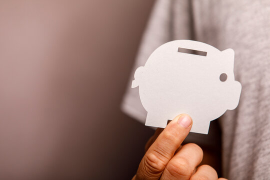A person holds a white paper piggy bank cutout, representing financial savings and investment.