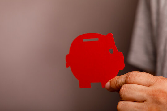 A person's hand holds a vibrant red piggy bank cutout, representing financial savings and