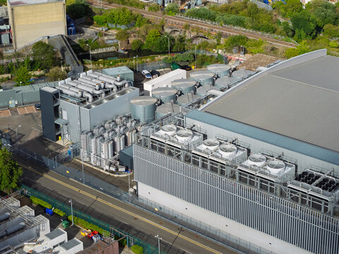 Aerial view of a data center facility featuring industrial cooling units, ventilation systems, and technical infrastructure surrounded by greenery and a railway line in the United Kingdom.