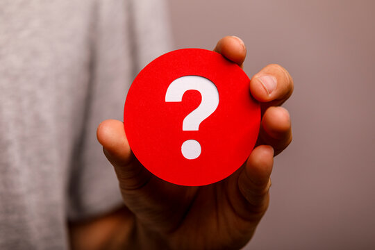 A person's hand holds a vibrant red circle with a white question mark, symbolizing questions.