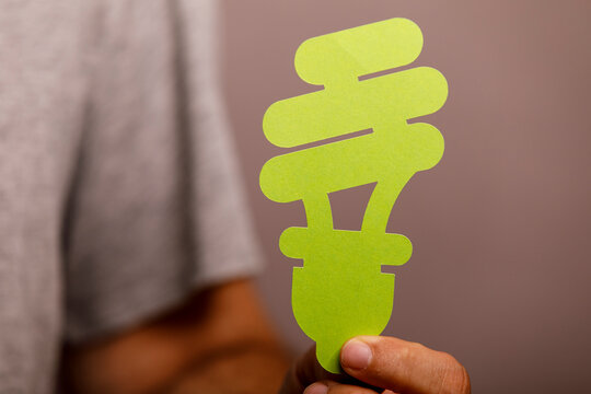 A hand holds a green paper cutout of an energy-efficient light bulb, symbolizing eco-friendly