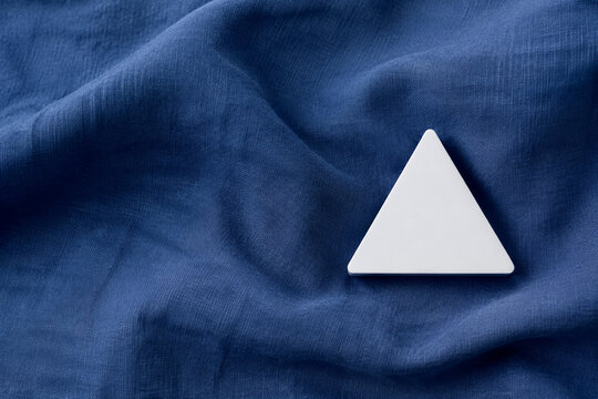 Single white equilateral triangle object on deep blue linen, calm still life for editorial concept