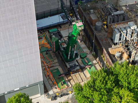 Aerial view of a green mobile crane positioned at a data center construction site, featuring industrial equipment, metal structures, and surrounding green trees in the United Kingdom.