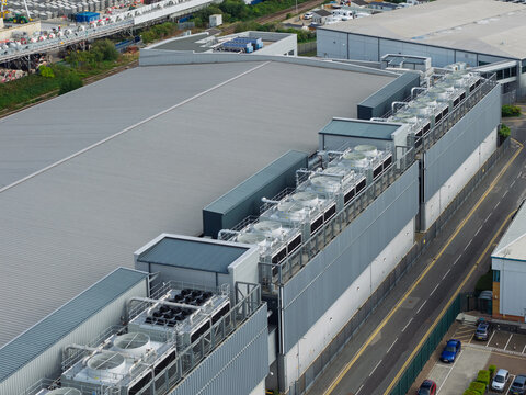 Aerial view of a data center featuring large industrial cooling units on the roof, situated next to a road and adjacent warehouse buildings in the United Kingdom.
