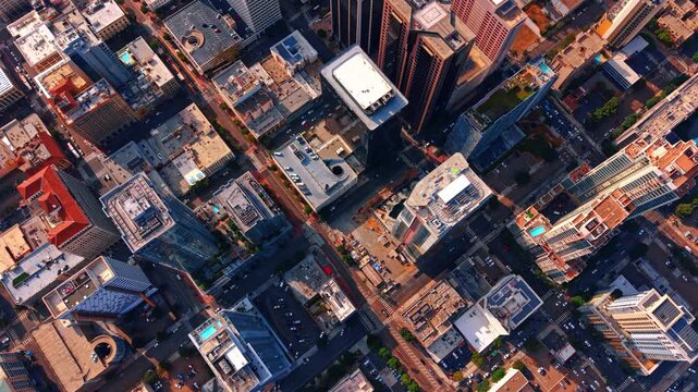 Diagonal street grid and rooftops viewed above San Diego. Sunlit buildings and crosswalks form intersecting lines around shaded streets in central San Diego.