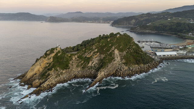 Aerial view of Getariako Itsasargia lighthouse on the rocky San Anton hill, surrounded by the Cantabrian Sea, with the harbor and town of Getaria Getaria, Euskadi, Spain.