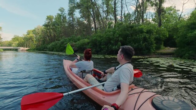 Middle-aged couple navigating tandem kayak on calm river water during summer holiday