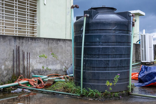 Large black plastic water storage tank installed on residential building rooftop. Utility plumbing system outdoors.