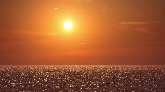 Bright golden sun setting over calm ocean horizon for peaceful sunset concept