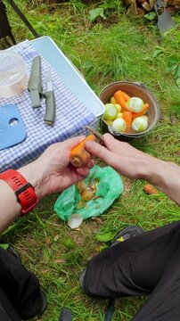 POV male hands peeling a raw carrot with peeler at an outdoor camping picnic