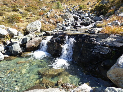 A river in the Alps in the fall with small waterfalls. On a sunny day, rocks lie beneath clear mountain water. The river is located in the Valzifenz Tal  in the Austrian alps.