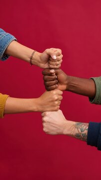 Diverse multiethnic group of friends stacking fists in unity and teamwork gesture against red background