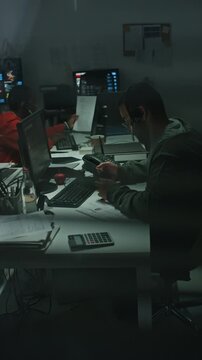Vertical video of young biracial man wearing headset using smartphone at computer. Footage fits projects on cyber security, call center operations, fraud investigation and night tech support