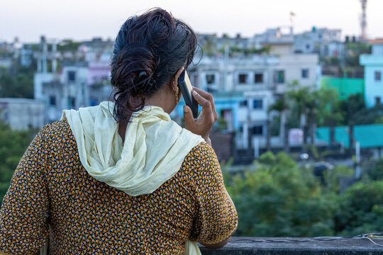 Back view of a woman talking on a mobile phone outdoors on a rooftop. Asian woman communicating on cellular smartphone in city setting.
