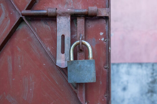 Heavy metal padlock locking rusted iron door latch outdoors in daylight. Security protection system for residential entrance gate.