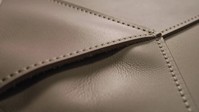 Shifting camera showing stitched leather panel in studio, highlighting triangular flap stitching