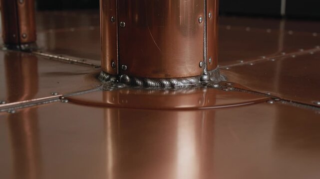 Heating copper joint at column base melting outward for joining panels in workshop, showing rivets