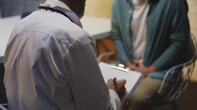 Urologist takes notes while male patient describes symptoms at check-up