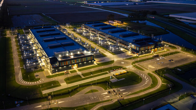 Aerial view of the Microsoft Data Center illuminated at night, featuring large industrial buildings, parking areas, and surrounding landscape in Middenmeer, North Holland, Netherlands.