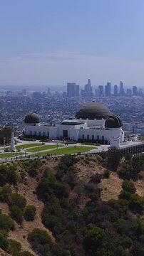 Aerial perspective looking over Griffith Observatory on Mount Hollywood with visitors walking around the grounds and the Los Angeles skyline visible beyond.