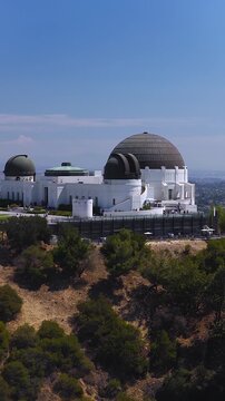 Aerial view moves towards the historic Griffith Observatory situated on the slopes of Mount Hollywood in Griffith Park, Los Angeles, on a bright sunny day.