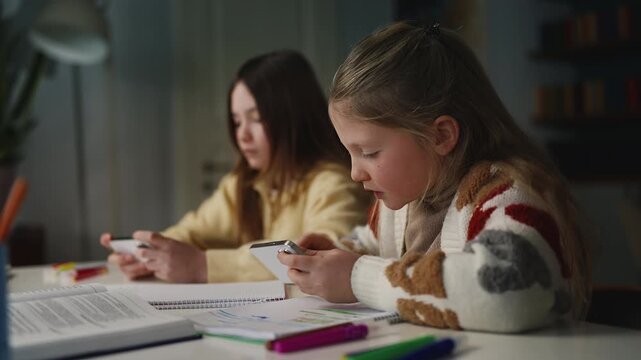 Girl and her friend play games on their phones instead of studying at home