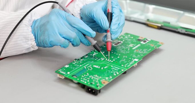 Close-up of a technician in blue gloves testing a green circuit board with multimeter probes on a workbench.