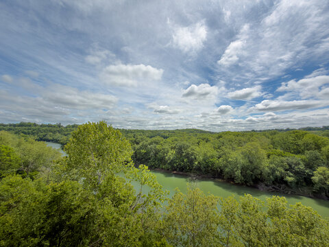 Wide-angle overlook of a bend in the Kentucky River,  framed by leafy treetops, wooded hills, and a dramatic sky of wispy cirrus and puffy white clouds