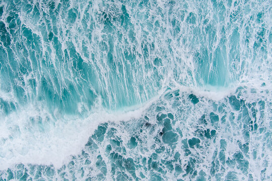 Aerial view of turquoise ocean waves with white foam crashing near the coast of Lofoten in Nordland, Norway.