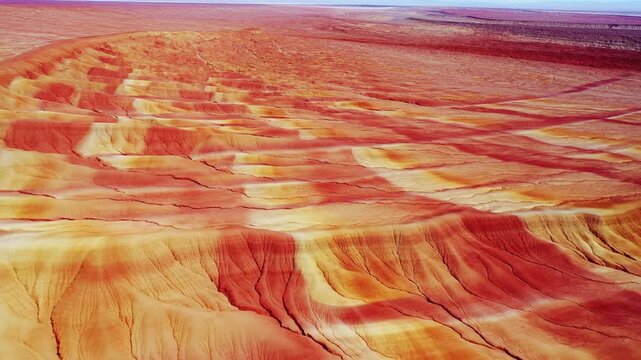 Aerial camera glides over a multicolored eroded desert landscape with layered rock formations. Nature documentaries, geology education, and earth science presentations.