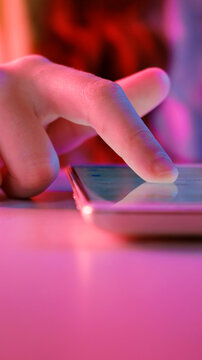 Use of mobile phone in trendy neon lights. Creative vivid color of ultraviolet red and blue. Hands of Teen Girl scrolling up photos Close-up at dark neon room. App for sale in shop, Social media.