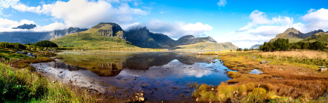 Panoramaview near Flakstadpollen with water, reflections, green mountains and low clouds in the impressive Lofoten landscape.