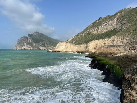 White surf rolling into a rocky cove beneath tall limestone cliffs at Mughsail, Dhofar, Oman