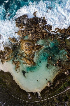 Aerial view of Two Peoples Bay Nature Reserve featuring turquoise waters, rugged granite boulders, white sand beach, and crashing waves in Albany, Western Australia, Australia.