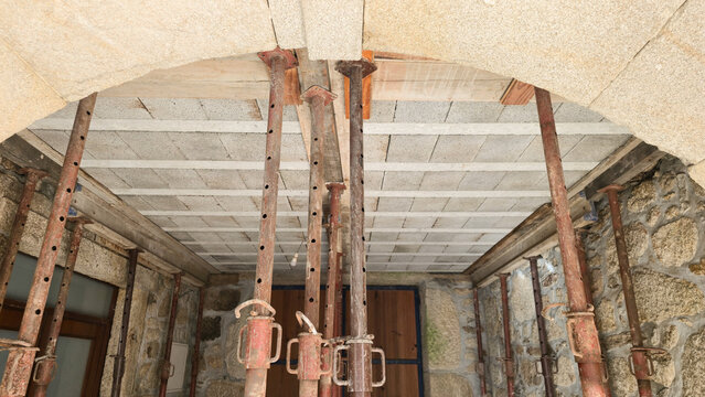 Adjustable steel props support a ceiling during structural home renovation. Concepts: construction safety, temporary support, building repair, structural reinforcement.