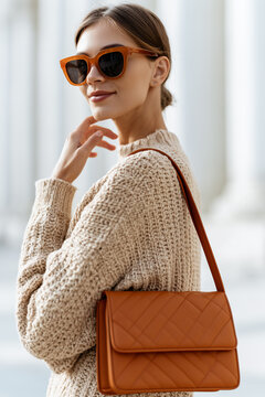 Trendy woman in sunglasses and beige knit sweater carrying a stylish quilted brown leather shoulder bag.