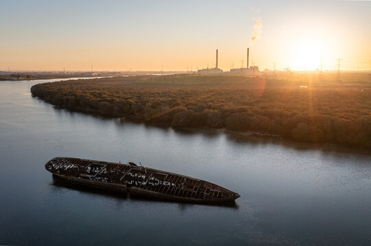Aerial view of the rusted Santiago shipwreck resting in the calm waters near mangroves with a power station in the background at sunset near Port Adelaide, South Australia, Australia.