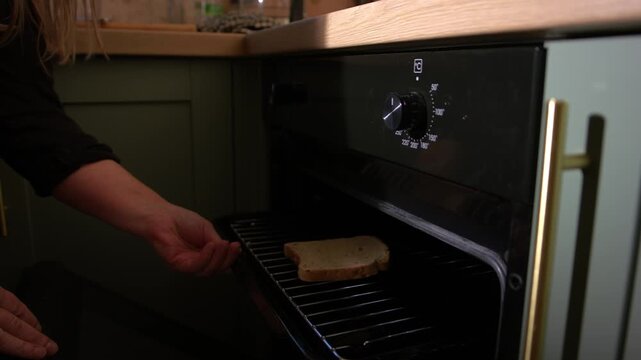 Woman putting slice of bread in oven grill to make toast