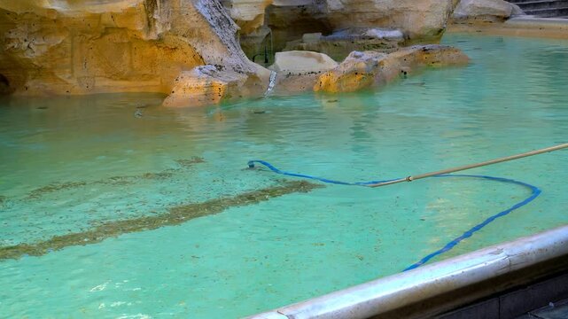 Rome, Italy. Cleaning up thrown coins into the fountain. Trevi Fountain - Sculptural fountain in the Rococo style, built by N. Salvi in 1762. Summer day