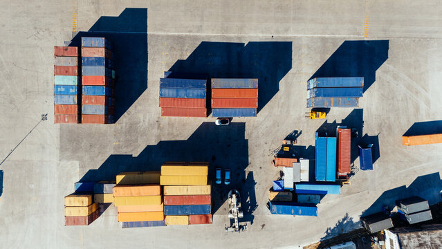 Aerial view of colorful shipping containers stacked in a logistics yard with long shadows cast on the concrete ground in Indjija, Vojvodina, Serbia.