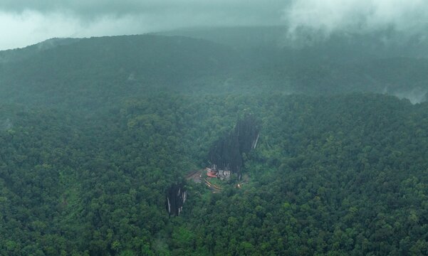 Aerial view of the unique karst rock formations of Yana Caves surrounded by dense lush green forest under a cloudy sky in Yana, Karnataka, India.