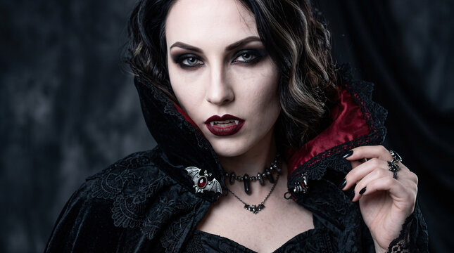 Gothic vampire woman in black costume with red collar, fangs and dark makeup for halloween theme