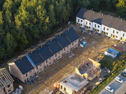 Aerial view of a residential construction site with rows of terraced houses in various stages of completion, near trees and a parking area in Wieliczka, Lesser Poland Voivode, Poland.