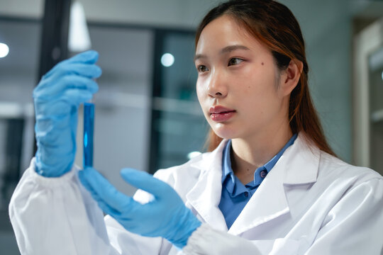 Young Asian scientist examining blue liquid in test tube during laboratory experiment analysis