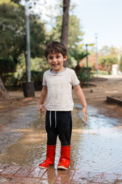 Happy child playing in mud puddle wearing red boots